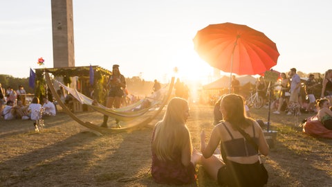 Sommerzeit ist Festivalzeit. Im Bild Menschen auf einem Festival beim Sonnenuntergang. 