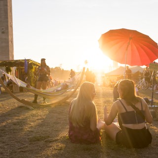 Sommerzeit ist Festivalzeit. Im Bild Menschen auf einem Festival beim Sonnenuntergang. 