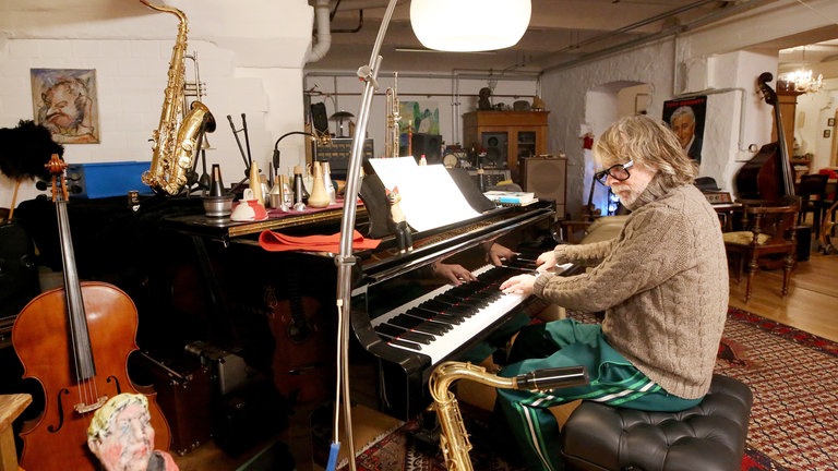 Helge Schneider sitzt am Piano, umgeben ist er von schier unzähligen Instrumenten. 