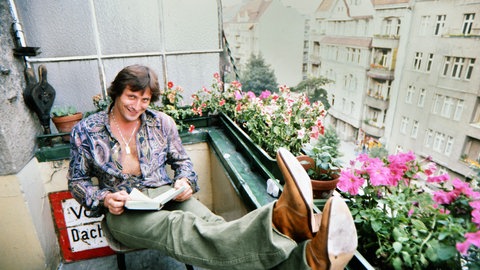 Konstantin Wecker 1977 in München auf einem Balkon sitzend.