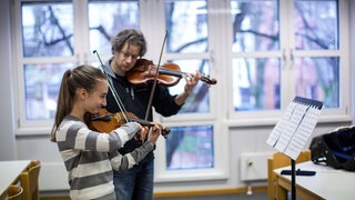Ein Musikschullehrer mit einer Schülerin beim Geigenunterricht