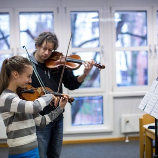 Ein Musikschullehrer mit einer Schülerin beim Geigenunterricht