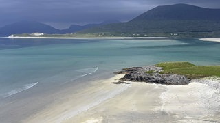 Dramatischer Himmel über einem ruhigen Strand mit türkisfarbenem Wasser und Bergen im Hintergrund, Äussere Hebriden (Isle of Harris, Schottland, Großbritannien)