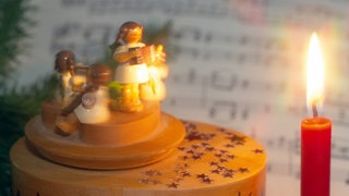 Symboldbild Weihnachtslieder: Weihnachtsspieluhr neben einer brennenden Weihnachtskerze