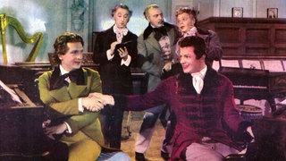 Farb-Werbefoto für den Film "Polonaise" ("A Song to Remember", USA 1945). Franz Liszt (Stephen Bekassy) und Frédéric Chopin (Cornel Wilde) sitzen Rücken an Rücken am Piano und reichen sich freundschaftlich die Hand.