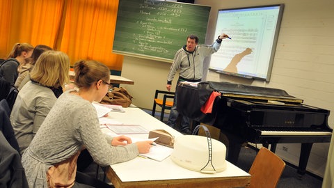 Musikunterricht am Gymnasium Holthausen: Jugendlicher an der Tafel erläutert eine Partitur.