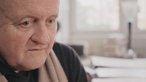 Wolfgang Rihm blickt ernst in den Raum. Detailaufnahme seines Gesichts.