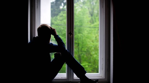 Symbolbild Einsamkeit: Ein Mann sitzt alleine an einem Fenster und schaut nach draußen