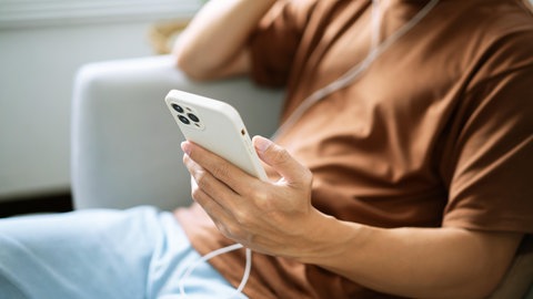 Ein junger Mann hört mit Kopfhörern Musik auf seinem Smartphone | Urheberrecht: Was KI-generierte Musik so problematisch macht