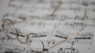 Symbolbild Musik komponieren: Eine Lesebrille liegt auf einem Notenblatt