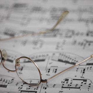 Symbolbild Musik komponieren: Eine Lesebrille liegt auf einem Notenblatt