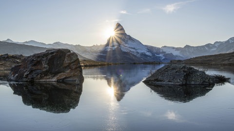 Matterhorn und Spiegelung im Stellisee bei Sonnenuntergang. Die Sonne geht hinter dem Berg unter. 