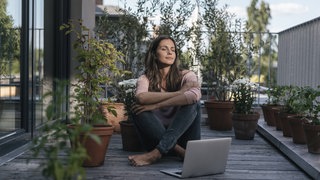 Frau mit Laptop sitzt auf Balkon