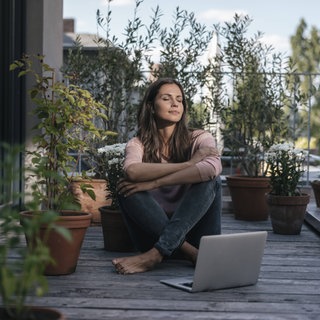 Frau mit Laptop sitzt auf Balkon
