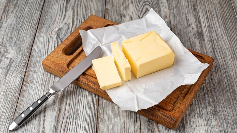 Frische Butterscheiben auf einem Holzbrett mit einem Buttermesser, bereit zum Bestreichen.