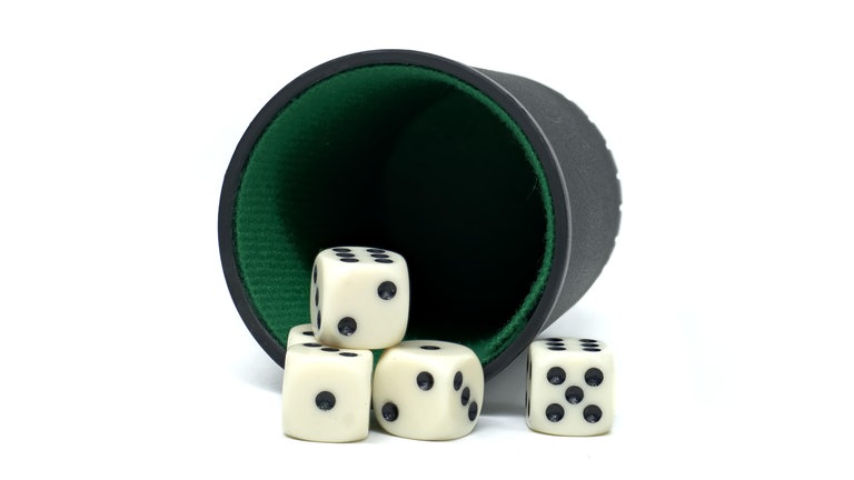 Vier Würfel, die aus einem grün-schwarzen Becher gefallen sind.