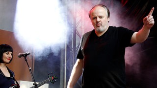"Sternenhimmel"-Sänger Hubert Kah singt auf einer Bühne mit erhobenem linken Arm seine Lieder.