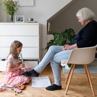 Mädchen spielt Flöte, die Großmutter sitzt vor ihr