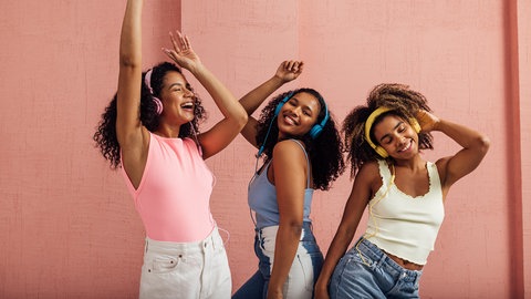 Drei junge Frauen hören über Kopfhörer Musik und tanzen dabei