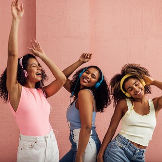 Drei junge Frauen hören über Kopfhörer Musik und tanzen dabei