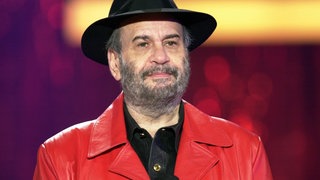 Drafi Deutscher singt Lieder wie "Marmor, Stein und Eisen bricht" mit roter Jacke und schwarzem Hut.
