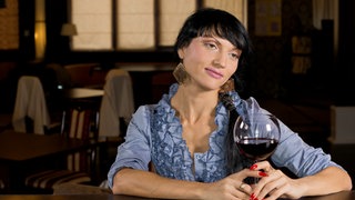 Symbolbild für eine Listening Bar: Eine Frau sitzt mit einem Glas Wein an einer Theke und hört achtsam zu