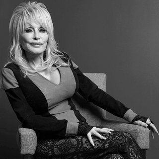 Sängerin Dolly Parton sitzt auf einem Stuhl und schaut in die Kamera.