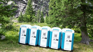 Mehrere ToiToi-Toilettenhäuschen im Gebirge: Woher kommt der Ausdruck toi, toi, toi, mit dem man jemandem Glück wünscht?