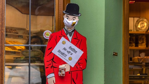 Ein Pappaufsteller zeigt einen Mann mit schwarzer Melone auf dem Kopf und rotem Jackett vor einer Bäckerei. In der Hand hält er ein Schild "Kaffee für uff d'Stroß", also "Coffee to go" in badischer Mundart: Dialekte wirken unterschiedlich sympathisch oder unsympathisch; das zeigen Umfragen immer wieder. Mehrere Faktoren spielen dabei eine Rolle