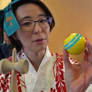 Eine Frau im Kimono zeigt das japanische Spiel "Kendama"