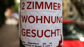 Auf einem Zettel für ein Wohnungsgesuch an einem Laternenpfahl in der Südstadt in Köln steht „2 Zimmer Wohnung gesucht!“ Die Wohnungskrise spitzt sich aus Sicht von Mieterschützern, Wohlfahrtsverbänden und Gewerkschaften zu.