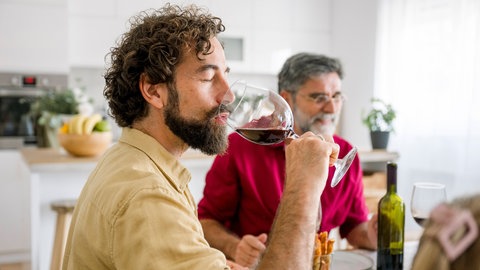 Mann trinkt Rotwein am Essenstisch. Auch das "gesunde Glas Rotwein" ist ein irreführender Mythos.