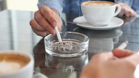 Zigarette, Aschenbecher auf Café-Tisch. Kaffee sorgt nicht für ein erhöhtes Lungenkrebsrisiko - der Zusammenhang ist irreführend.