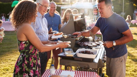 Ein Mann bedient Gäste bei einem Grillfest | Tipps für Hochzeiten und Co: So könnt ihr schön feiern und trotzdem sparen