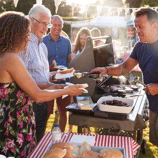 Ein Mann bedient Gäste bei einem Grillfest | Tipps für Hochzeiten und Co: So könnt ihr schön feiern und trotzdem sparen