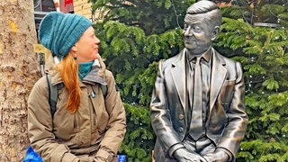 SWR1 Neuanfang: Heike sitzt auf einem Londoner Weihnachtsmarkt neben der metallenen Statue von "Mr. Bean". 