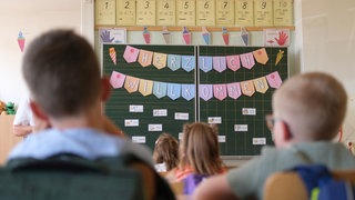 Erstklässler sitzen in ihrem Klassenzimmer. Lehrkräfte und Eltern können bei der Motivation zum Lernen helfen.