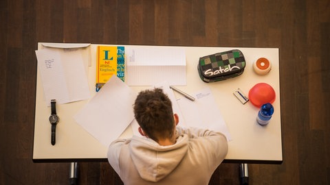 Schüler mit Heft, Mäppchen und Büchern am Schreibtisch. In diesen Tagen schreiben viele Schülerinnen und Schüler ihr Abitur. Wie wichtig sind die Abiturnoten heute noch?