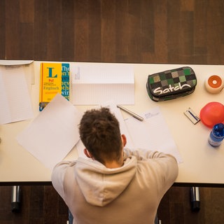 Schüler mit Heft, Mäppchen und Büchern am Schreibtisch. In diesen Tagen schreiben viele Schülerinnen und Schüler ihr Abitur. Wie wichtig sind die Abiturnoten heute noch?