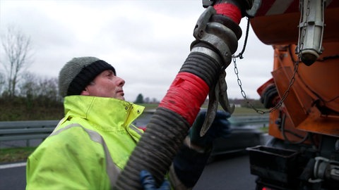 Ein Mitarbeiter der Straßenmeisterei Langenau befestigt einen Schlauch am orangenen Spülwagen.