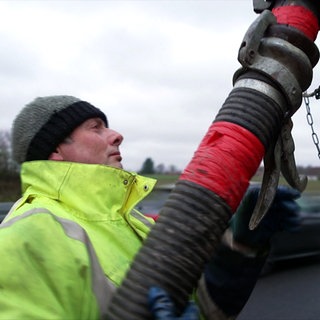 Ein Mitarbeiter der Straßenmeisterei Langenau befestigt einen Schlauch am orangenen Spülwagen.