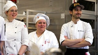 Die Konditoren-Azubis Katrin Jenne, Alla Damm und Karam Hakkou tragen Schürzen und Mützen.