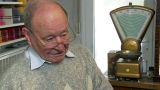 Der 87-jährige Heinz Rittberger steht in seinem Seifenladen in Stuttgart. Neben ihm steht eine Waage.