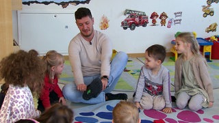 Erzieher Andrés sitzt in der Kita inmitten von Kindern.