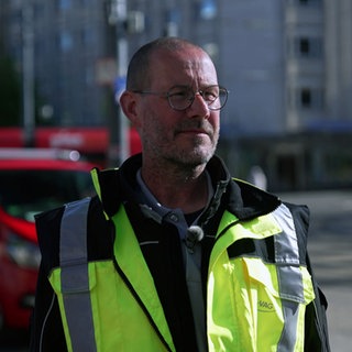 Edgar Schultz überwacht das Liniennetz der Freiburger Verkehrsbetriebe VAG. Er steht auf der Straße und trägt eine gelbe Warnweste.