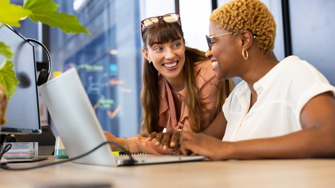 Zwei Kolleginnen lächeln sich an | Sind Freundschaften am Arbeitsplatz schlecht für das Team?
