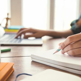 Frau tippt auf ihrem Laptop und schreibt in ein Notizbuch 