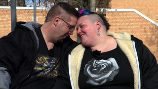 Lukas und Kathi aus Ostfildern sitzen auf einer Bank im Freien und lehnen verliebt die Köpfe aneinander.