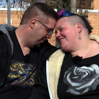 Lukas und Kathi aus Ostfildern sitzen auf einer Bank im Freien und lehnen verliebt die Köpfe aneinander.