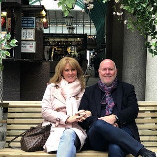 Kim und Christian sind seit 36 Jahren ein Paar. Sie sitzen nebeneinander auf einer Holzbank.